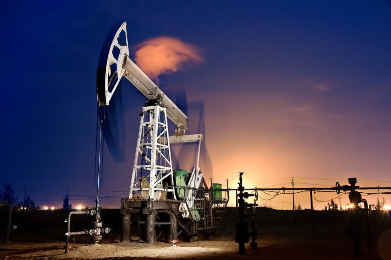 The image depicts an oil pump jack in operation, with gas torches illuminating the scene. It was taken at night using a long exposure technique.