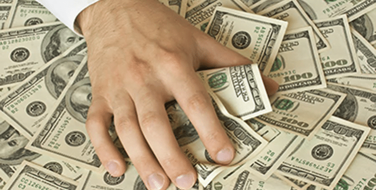 The image depicts a hand grasping U.S. dollars.