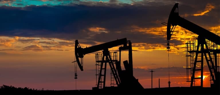 The image depicts oil pumps on an oil rig against a sunset background.