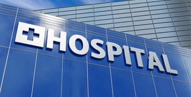 The image depicts the facade of a hospital in a commercial and business district under a blue sky.