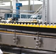 The image shows a cooking oil bottle moving along a factory production line.