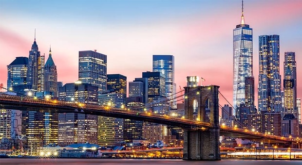 The image depicts the Brooklyn Bridge and the Lower Manhattan skyline under a purple sunset.